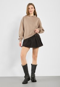 Khaki oversize dukserica s dugim rukavima, u kombinaciji s crnom traper minjakom nabranom u struku i crnim kožnim čizmama do koljena s metalnim akcentima.