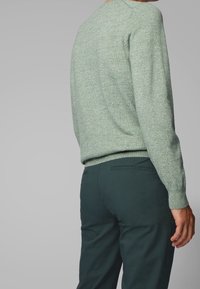 Jasnozielony sweter o fakturze, z okrągłym dekoltem, w zestawie z ciemnozielonymi dopasowanymi spodniami. Sweter ma prążkowane mankiety i dół.