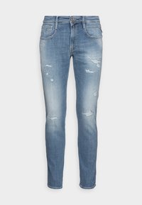 Jeans ajustados de color azul claro con parches desgastados y decoloración, que cuentan con bolsillos frontales y traseros y un cierre de botón y cremallera.