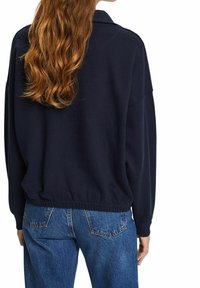 Sudadera azul marino con un corte relajado, dobladillo acanalado y hombros caídos, combinada con jeans de mezclilla azul claro. Textura de tela suave.