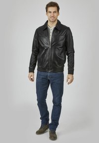 Črna usnjena bomber jakna z zadrgo, rebrastimi manšetami in robom, v kombinaciji z modrimi jeans hlačami in rjavimi čevlji na vezalke.
