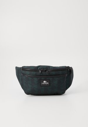 Sac banane Lacoste Sport vert foncé avec motif géométrique noir, deux compartiments zippés et écusson logo à l'avant.