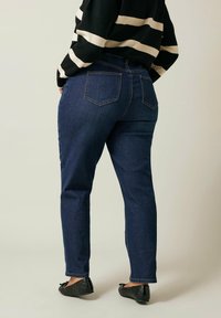 Tummansiniset farkut, joissa on kapea malli, viisi taskua ja klassinen vyötärö, yhdistettynä mustiin tikkivuorattuihin balettikenkien ja musta-beige-raitaiseen neulepaitaan.