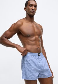 Ανοιχτό μπλε μπόξερ με σχέδιο και ελαστική μέση που φέρει μαύρη ετικέτα λογότυπου. Το ύφασμα φαίνεται λείο με διακριτική υφή.