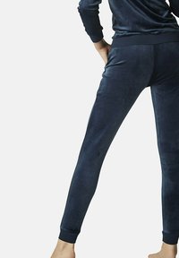 Pantalon de survêtement en velours bleu marine avec une coupe slim, taille élastique et poignets côtelés, présentant une texture douce et sans motifs visibles.