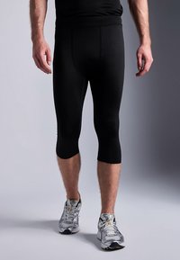 Svarta atletiska leggings med en slät yta, längd ovanför knäna och en figurnära design, kombinerade med gråa löparskor.