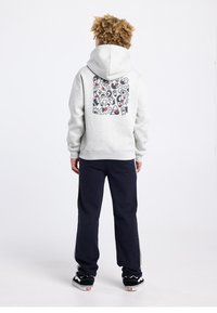 Sweat à capuche gris avec un motif graphique au dos, associé à un pantalon de survêtement bleu marine et des chaussures noires avec des accents blancs.