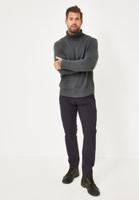 Grauer Rollkragenpullover mit gerippten Akzenten, kombiniert mit dunkler Hose und schwarzen Schnürstiefeln. Unifarbe, strukturierter Stoff, lässige Passform.