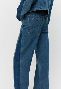 Jeans in denim blu con vestibilità relax, pannello laterale a contrasto e tasche posteriori standard con un sottile design ricamato.