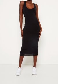 Schwarzes Tankkleid mit Rundhalsausschnitt und figurbetonter Silhouette, aus glattem Stoff, kombiniert mit weißen Sneakers.
