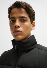Black puffer jacket with a high collar and front zipper. Material appears textured, with subtle stitching details on the shoulders.