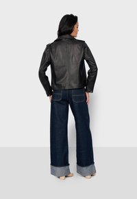 Veste en cuir noir avec une coupe courte, des revers larges et des manches zippées, associée à un jean en denim foncé taille haute et des sabots en bois.