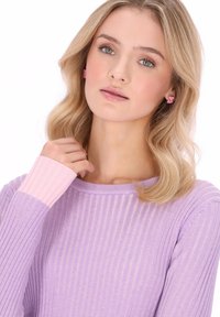 Lila gerippter Pullover mit rosa Akzent an den Ärmeln, mit einem runden Ausschnitt. Das Model hat welliges Haar und trägt kleine rosa Ohrringe.