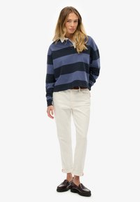 Polo de manga larga a rayas azul marino y azul claro combinado con pantalones crema de corte estrecho y mocasines oscuros, con puños enrollados.