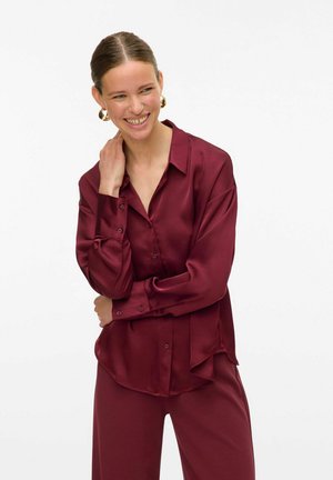 Burgundy satin shirt with a relaxed fit, long sleeves, and a pointed collar. Features button closure and side slits for added detail.