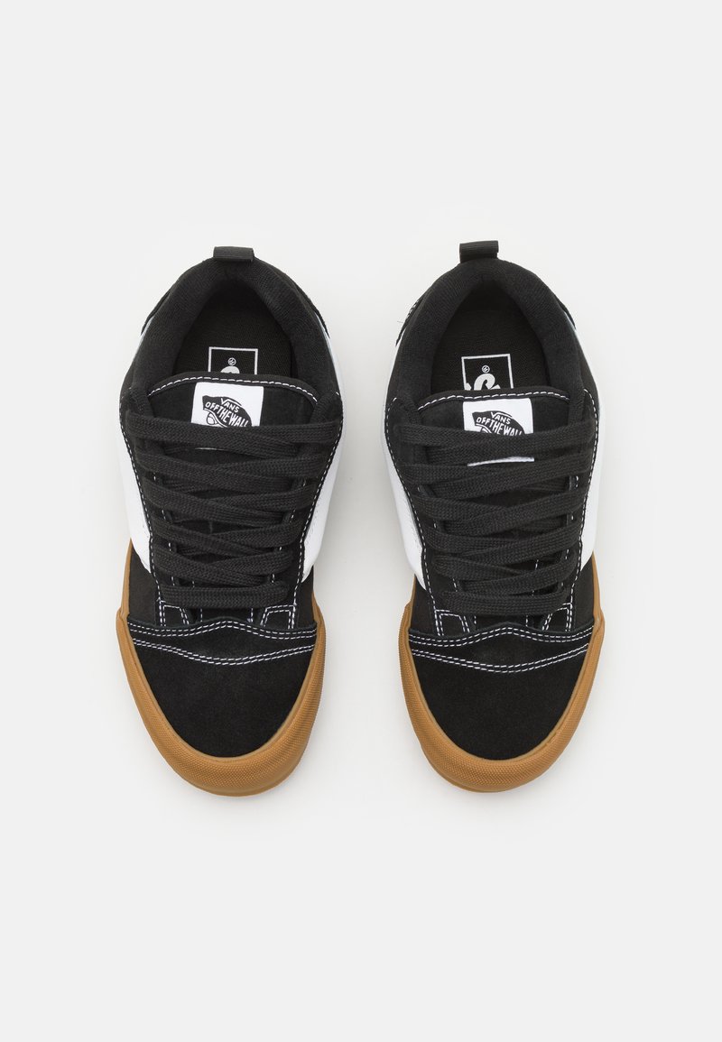 Sneaker in suede nero con accenti bianchi, punta rotonda e suole in gomma color caramello. Presentano lacci neri e dettagli di cucitura lungo i lati.