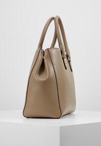 Sac à main en cuir beige à la forme structurée, doté de deux poignées supérieures, d'une texture subtile et d'accents discrets en métal doré le long de l'ouverture.