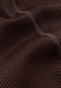 Brauner gerippter Stoff mit strukturierter Oberfläche. Das Material zeigt auffällige vertikale Linien und sichtbare Nähte entlang der Kanten.