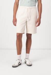 Lyse beige shorts med elastisk talje og snøre; lavet af blødt stof, der går til midt på låret, stylet med sidelommer.