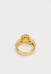 Anillo de oro con una banda gruesa que presenta una parte superior decorativa en forma de concha, fotografiado sobre un fondo blanco.