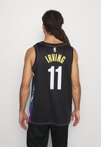 Man with dreadlocks wearing black NBA jersey with "IRVING" and number 11 seen from the back against a plain background.