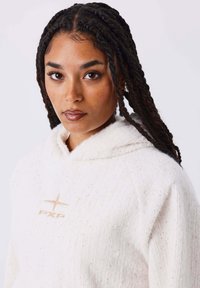 Sudadera blanca texturizada con capucha, que presenta un sutil patrón moteado y un logo "PXP" en color beige claro en el pecho.