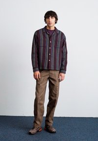 Button-up shirt with purple and multi-colored stripes, paired with brown pants and dark sneakers. Two chest pockets visible.