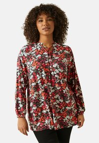 Kukallinen paita pitkillä hihoilla, avainaukko kauluksessa ja nyöri punaisilla, valkoisilla ja violetilla kukilla mustalla taustalla. Pehmeä kangas, rento istuvuus.