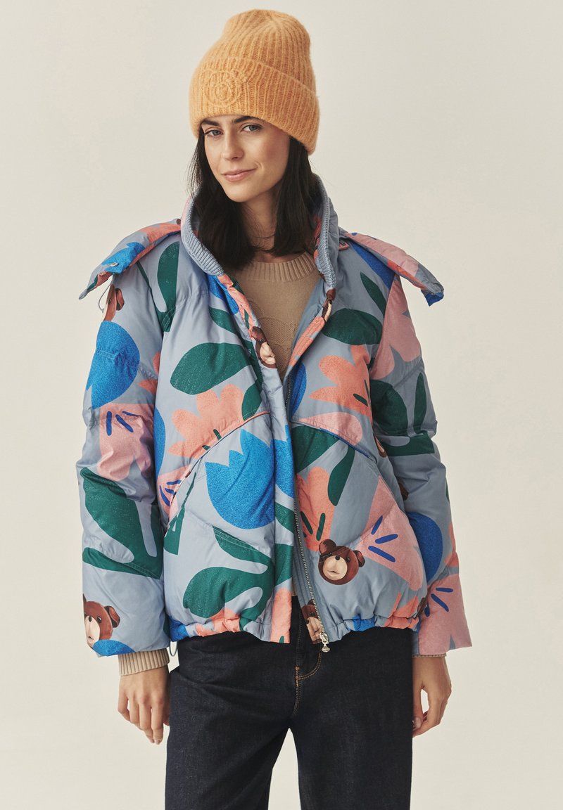 Farverig pufferjakke med blomsterprint i blå, pink og grøn. Har en indsnævret talje, lynlås-lukning og hætte. Matcher med en orange hue.