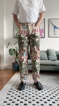Pantalones con patrón de camuflaje en tonos tierra con escenas de figuras. Fabricados en una tela con acabado texturizado, cuentan con bolsillos y un corte recto.