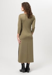 Vestido midi verde oliva con mangas tres cuartos, diseño ajustado, abertura lateral y textura suave. Combinado con botines negros.