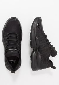 Baskets de sport noires avec une finition lisse et brillante, des panneaux en maille texturée et un système de laçage élastique. Semelles rembourrées pour plus de confort.