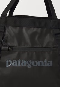 Fekete szövet táska textúrázott felülettel, cipzáras zsebbel és szürke "patagonia" logóval. Strapabíró fekete füllel.