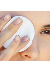 Rund vit bomullspad hålls mot huden, med en hand som har ljus, naturlig nagellack. Närkamera vy som fokuserar på produktens textur och användning.