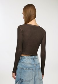 Brązowy, długi rękaw, krótki top z okrągłym dekoltem, w połączeniu z wysokim stanem jasnoniebieskimi dżinsowymi szortami z dużymi tylnymi kieszeniami.