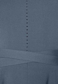 Modrý pruhovaný pletený materiál s texturovaným povrchem; obsahuje svislý řádek drobných knoflíkových detailů podél zadní části a široký pasový lem.