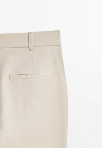 Pantalon beige clair avec une texture lisse, doté d'une taille et d'une poche arrière avec un design de rabat rectangulaire.