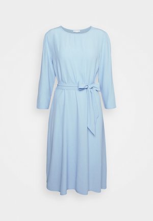 Jasnoniebieska sukienka do kolan z długimi rękawami, okrągłym dekoltem i kokardą zawiązaną w talii na jednolitym białym tle.