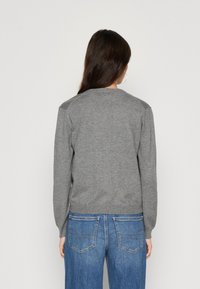 Sivkasta pleteno pulover s dolgimi rokavi, okroglo izrezano ovratnikom in rebrastim robom, kombiniran z svetlo modrimi jeans hlačami z zadnjimi žepi.