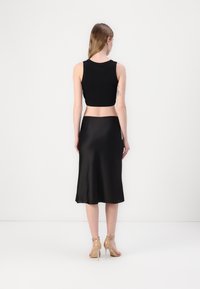 Svart ermeløs crop topp kombinert med et svart sateng midi skjørt. Skjørtet har en glatt tekstur og en subtil glans. Sandaler med klare stropper fullfører antrekket.