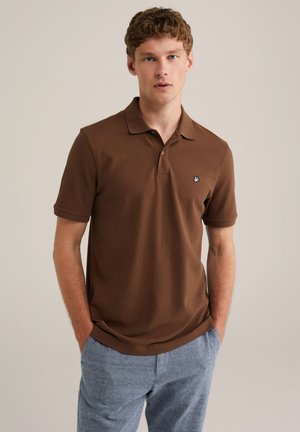 Brun kortärmad polo med krage, som har en liten broderad logotyp på vänster sida. Tyget har en mjuk textur.