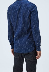 Laivastonsininen paita, jossa on pieni valkoinen pilkkukuvio, pitkät hihat, napilliset hihansuut ja suora helma. Valmistettu sileästä kankaasta.