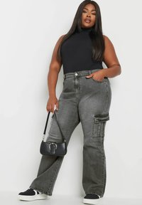 Pantalones cargo de pierna ancha gris con cintura alta, bolsillos frontales y detalle de bolsillo lateral, combinados con una blusa sin mangas negra y un bolso negro.