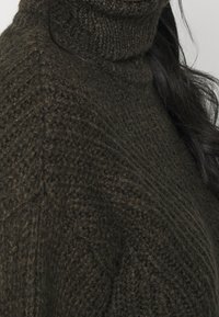 Maglione a collo alto di maglia verde scuro con motivo strutturato, caratterizzato da un collo alto e una vestibilità ampia, mostrato su uno sfondo neutro.