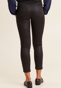 Jeans neri skinny con una texture liscia e elastica, dotati di vita media, due tasche posteriori e gambe tagliate e affusolate.
