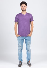 Purple short-sleeve v-neck t-shirt with a slightly faded texture, paired with light blue jeans and gray sneakers with white soles.