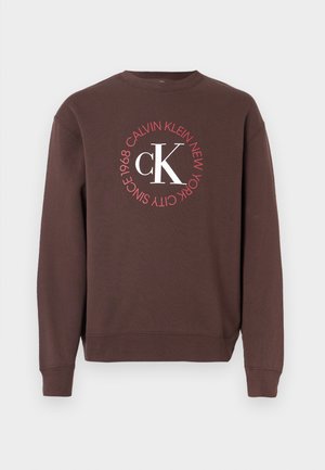 Brown sweatshirt with long sleeves, a crewneck, and a circular white and red graphic featuring "Calvin Klein New York 1968" and "CK".