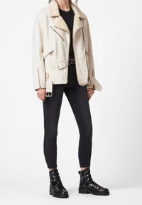 Giacca biker beige foderata in finta pelliccia, con numerose cerniere, abbinata a jeans skinny neri e stivali da combattimento neri con lacci.