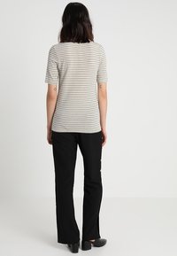 Camiseta de manga corta a rayas en beige claro y gris oscuro combinada con pantalones de pierna ancha negros con acentos de botones dorados. Zapatos negros simples.