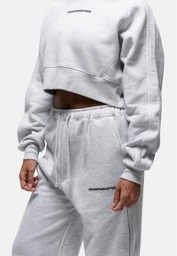 Felpa grigia tagliata e pantaloni abbinati in morbido tessuto. Caratterizzati da testo ricamato e vita elasticizzata. Design minimalista e vestibilità rilassata.